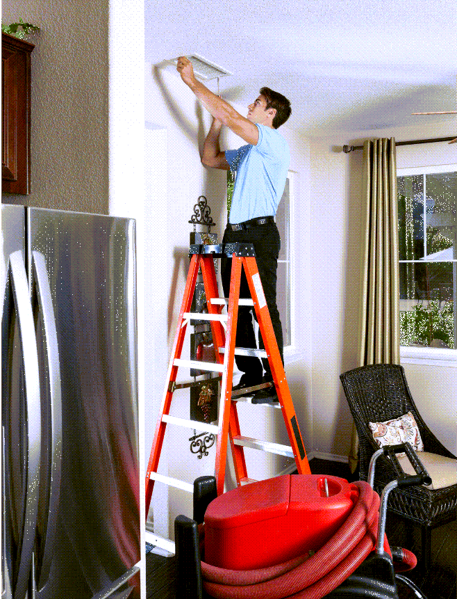 Technician on ladder cleaning air duct in home